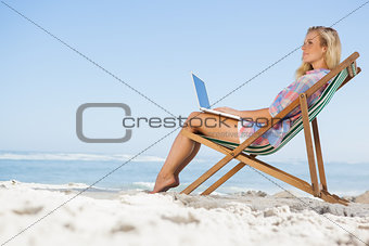 Pretty blonde sitting on beach using her laptop