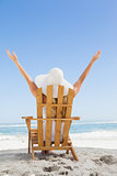 Woman sitting in deck chair at the beach with arms up