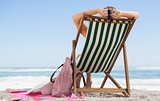 Woman sitting in deck chair at the beach with her beach bag and towel