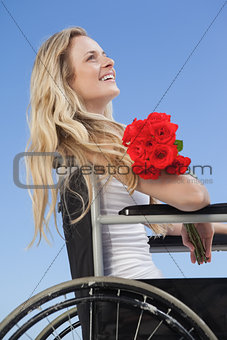 Wheelchair bound blonde smiling on the beach holding roses
