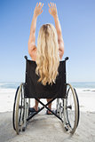 Wheelchair bound blonde sitting on the beach with arms up