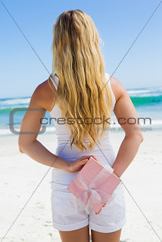 Blonde hiding present behind back on the beach