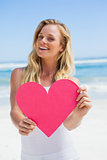 Smiling blonde showing pink heart on the beach