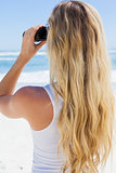 Blonde looking to the ocean through binoculars