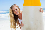 Blonde surfer holding her board smiling at camera