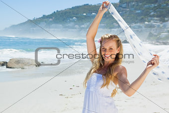 Pretty carefree blonde smiling at camera on the beach with scarf