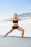 Fit blonde in warrior pose on the beach