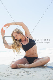 Fit blonde sitting in yoga pose on the beach