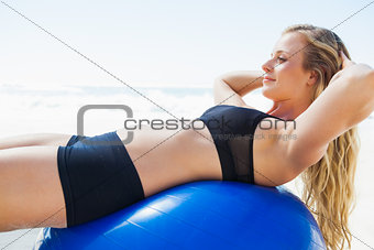 Fit blonde doing sit ups on exercise ball at the beach