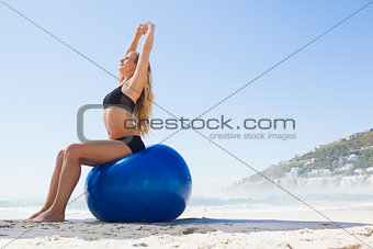 Fit blonde sitting on exercise ball at the beach