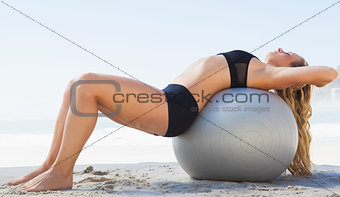 Fit blonde stretching her back on exercise ball at the beach