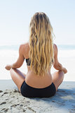 Fit blonde sitting in lotus pose on the beach