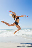 Fit blonde jumping gracefully on the beach
