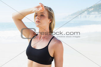 Fit blonde wiping her forehead on the beach