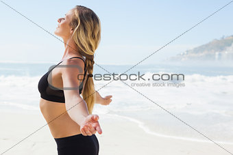Fit blonde standing on the beach with arms outstretched