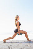 Fit blonde doing weighted lunges on the beach