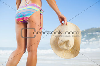 Lower half of fit woman holding sunhat on beach