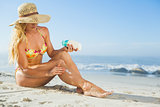 Gorgeous woman sitting on the beach in sunhat applying suncream
