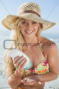 Pretty blonde sitting on the beach applying suncream