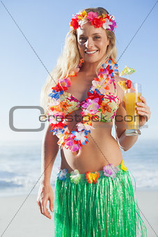 Gorgeous blonde in garland and grass skirt holding cocktail on the beach
