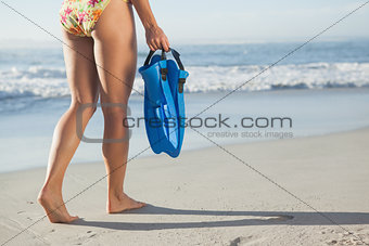 Woman holding flippers walking towards the sea