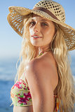 Gorgeous blonde in straw hat and bikini smiling at camera on beach