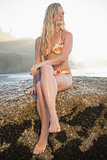 Gorgeous blonde in floral bikini sitting on a rock at beach