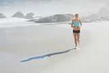 Fit woman smiling and jogging on the beach