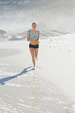 Fit woman jogging on the beach smiling at camera