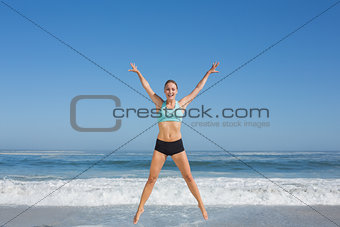 Fit woman jumping on the beach with arms out
