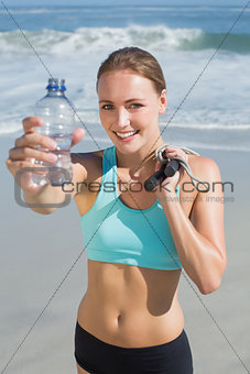 Fit woman standing on the beach holding water bottle and skipping rope