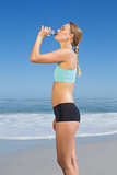 Fit woman standing on the beach drinking water