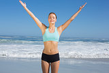 Fit woman standing on the beach with arms up