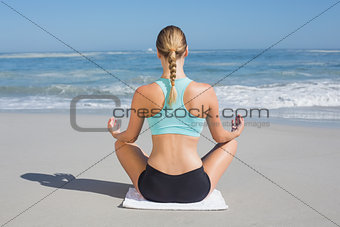 Fit woman sitting on the beach in lotus pose