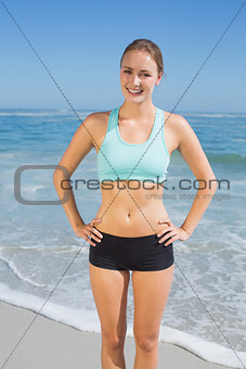 Fit woman standing on the beach with hands on hips