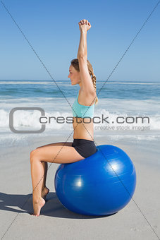 Fit woman sitting on exercise ball at the beach stretching arms