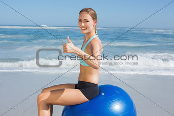 Fit woman sitting on exercise ball at the beach smiling at camera