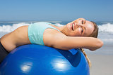 Fit woman lying on exercise ball at the beach stretching
