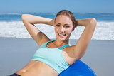 Fit woman lying on exercise ball at the beach doing sit ups