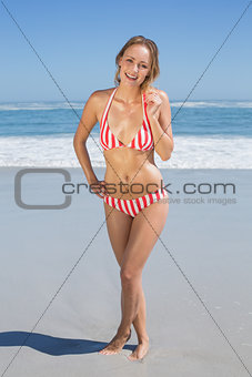Blonde fit woman in striped bikini at beach smiling at camera