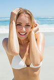 Beautiful blonde in white bikini smiling at camera on the beach
