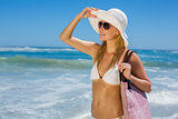 Smiling blonde in white bikini carrying bag on the beach