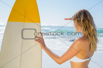 Blonde surfer in white bikini holding her board on the beach