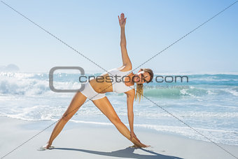 Gorgeous blonde standing in extended triangle pose by the sea