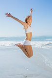 Gorgeous fit blonde jumping by the sea with arms out