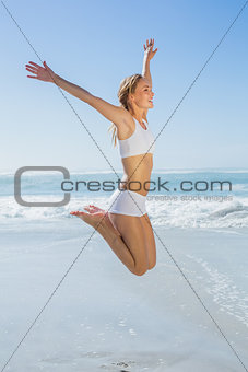 Gorgeous fit blonde jumping by the sea with arms out