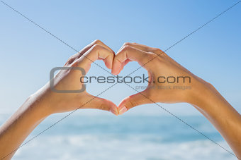 Female hands making heart shape by the sea