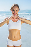 Gorgeous fit blonde making heart shape with hands by the sea