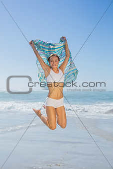 Gorgeous fit blonde jumping by the sea with scarf