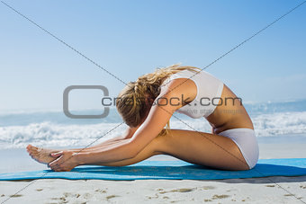 Gorgeous fit blonde in seated forward bend pose on the beach